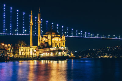 Illuminated ortakoy mosque with bridge in background in istanbul at night