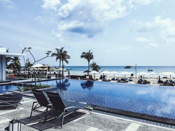 Palm trees by swimming pool against sky