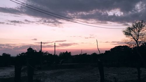 Silhouette trees and electricity pylons against sky during sunset