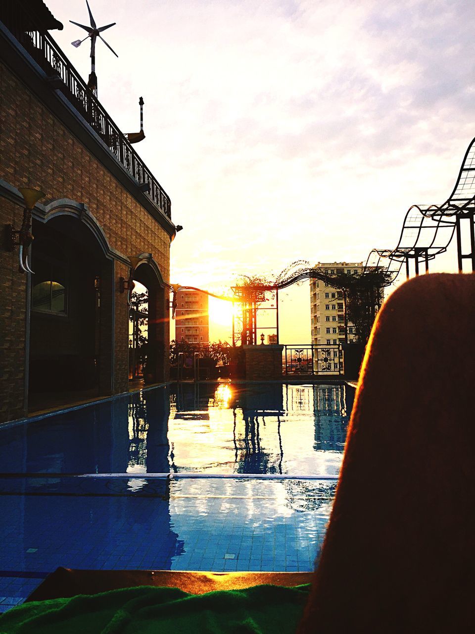 REFLECTION OF SILHOUETTE BUILDINGS IN SWIMMING POOL AGAINST SKY