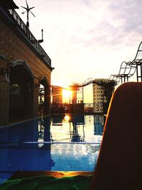 Reflection of silhouette buildings in swimming pool against sky during sunset
