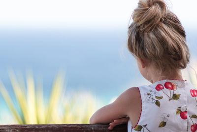 Rear view of girl with blond hair standing by railing