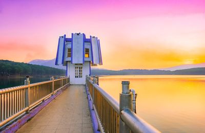 Built structure by lake against sky during sunset