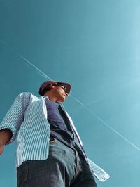 Low angle view of man looking away while standing against blue sky