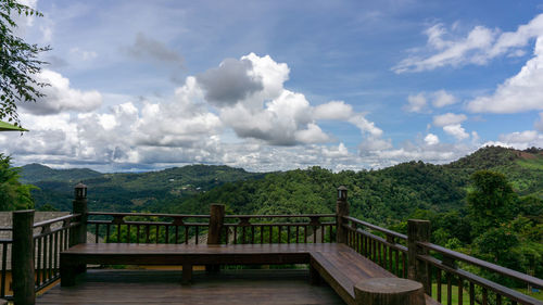 Scenery view from wooden terrace to white fluffy clouds on vivid blue sky above greenery mountain