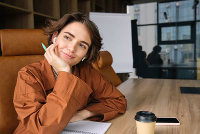 Portrait of young woman using mobile phone while sitting on table