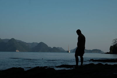 Silhouette man standing on sea against clear sky