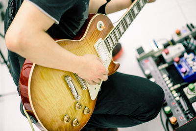 Midsection of man playing guitar at recording studio