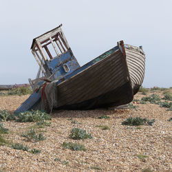 Abandoned boat on land against sky