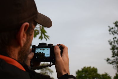 Rear view of man photographing through smart phone against sky