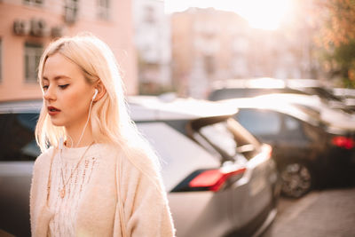 Young woman listening music on earphones while walking on city street