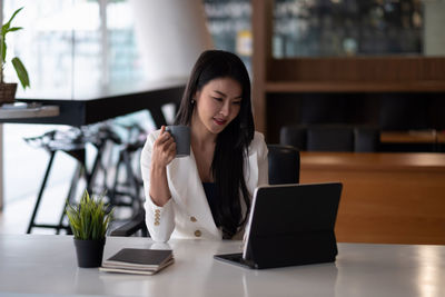 Young woman using phone while sitting on table