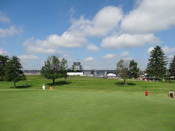 View of people on grassy landscape against cloudy sky