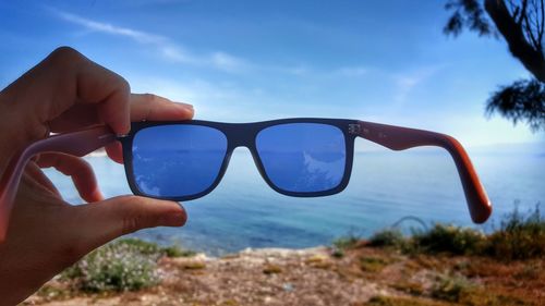 Close-up of person holding sunglasses against sea