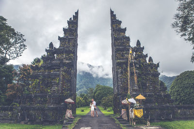 Couple on footpath at gate against sky