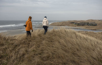 Rear view of couple walking on grass at beach