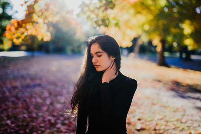 Young woman looking down while standing against trees in forest during autumn 