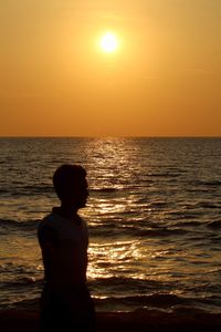 Silhouette man standing on beach against sky during sunset