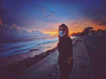 Woman standing on beach against sky during sunset