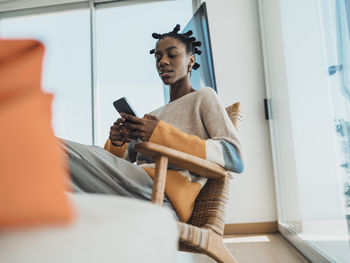 Young woman using smartphone sitting in armchair at home