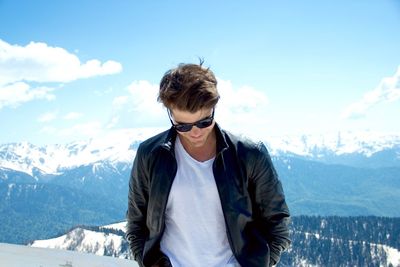 Young man wearing sunglasses standing on mountain against sky