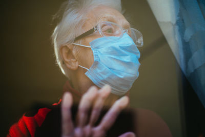 Close-up of senior woman wearing mask seen through window