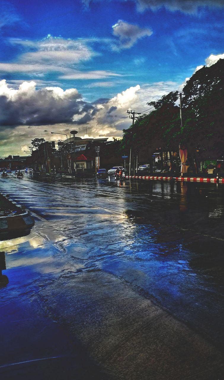 WET RIVER AMIDST ILLUMINATED CITY AGAINST SKY