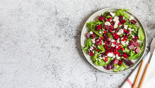 Arugula, beet and cheese salad with pomegranate and dressing on plate on grey stone kitchen table