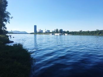 Scenic view of river by buildings against clear blue sky