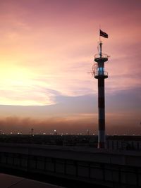 Lighthouse by building against sky during sunset