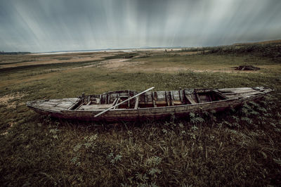 Abandoned boat moored on land against sky