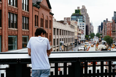 Rear view of teenage boy leaning on railing while standing in city