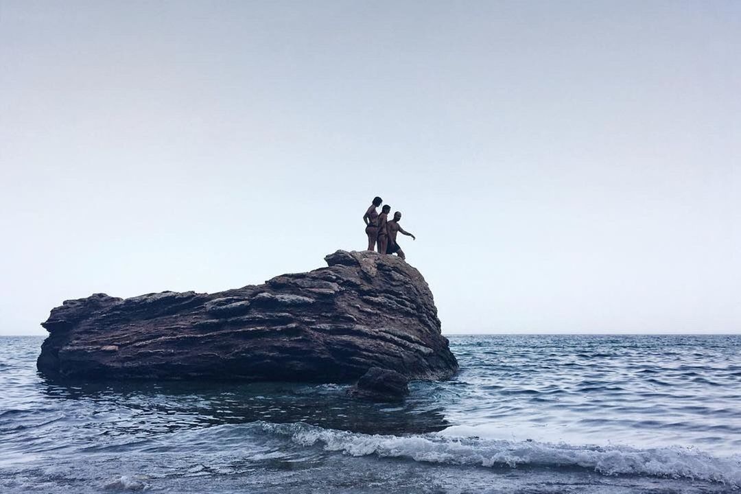 MAN STANDING ON ROCK AGAINST SEA