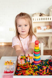 Portrait of cute girl sitting on table and playing with sensory bin with colored dyed pasta