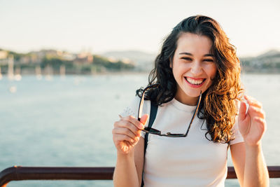 Portrait of a laughing girl holding the sunglasses by the sea at sunset