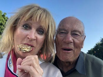 Portrait of senior woman eating food by man in park