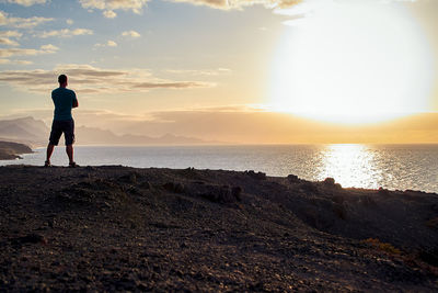 Rear view of woman walking on beach against sky during sunset