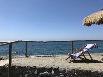 Deck chairs on beach against clear blue sky