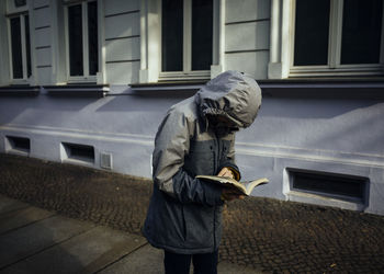 Man reading book while standing on footpath