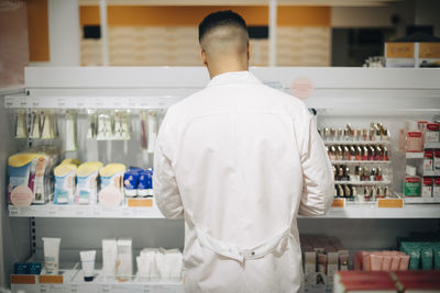 Rear view of male owner arranging medicines on rack at pharmacy store