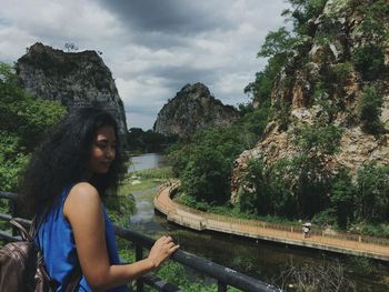 Woman standing on cliff by river against sky