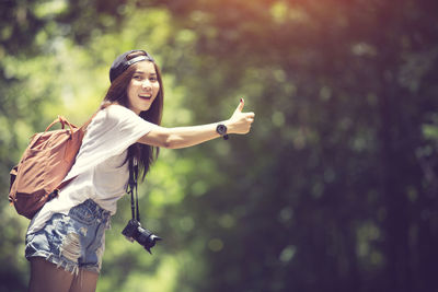 Portrait of smiling woman hitchhiking against trees