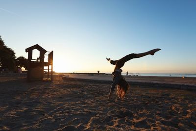 Woman performing handstand on shore against clear sky