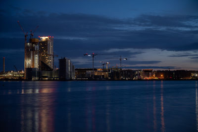 Illuminated buildings by sea against the sky at night