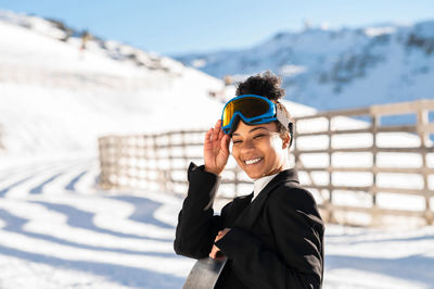 African american woman with goggles and a snowboard on a snowy mountain during winter