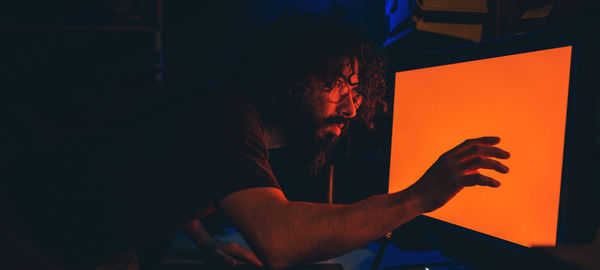 Man with curly hair and glasses, caught staring at an orange light on his monitor technology concept