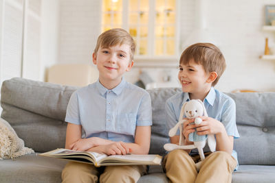 Two boys sitting on couch are reading book. older brother reads interesting