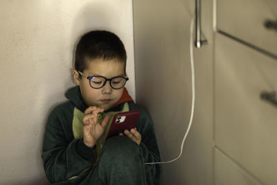 Closeup portrait of a boy who looks into the phone sitting on the floor, phone charging