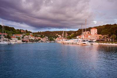 Sailboats moored at harbor against cloudy sky