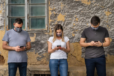 Full length of young man using mobile phone against wall